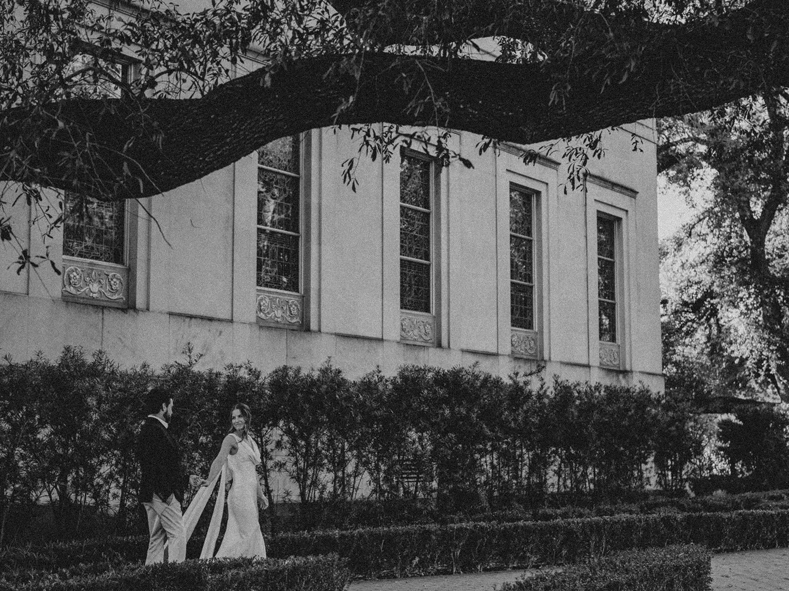 Wide exterior view of the Armstrong Browning Library at Baylor University with Natalie and Spencer walking together beneath the trees.