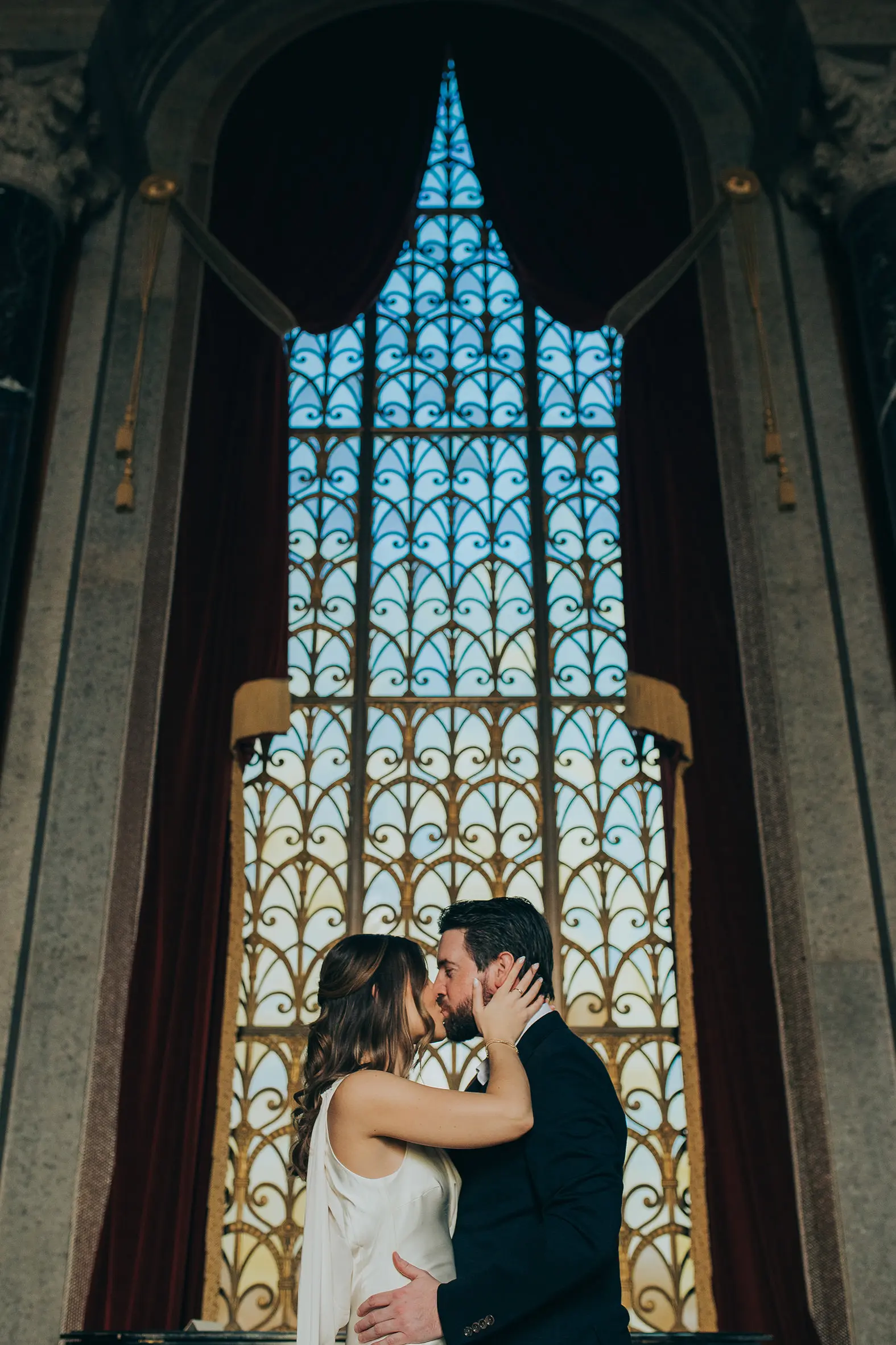 Natalie and Spencer sharing a kiss inside the Armstrong Browning Library in Waco Texas with dramatic stained glass behind them.