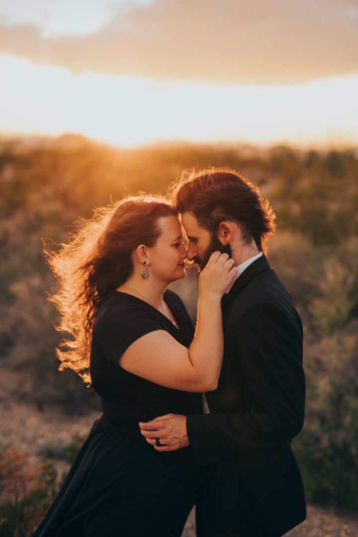 Engaged couple embracing in the golden desert light with her red hair flowing in the wind, intimate glowing sunset portrait in the Chihuahuan desert scrubland Big Bend National Park TX engagement photographer